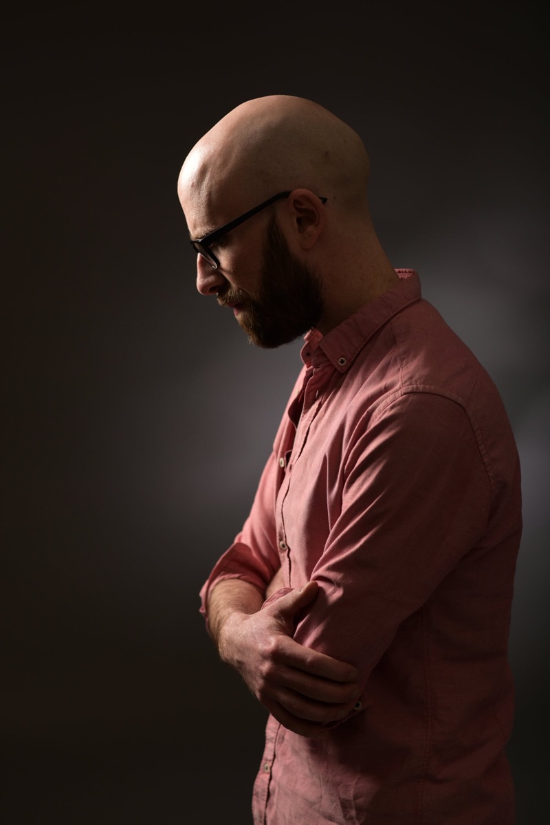 Simon Whistler, wearing glasses and a pink shirt, with his arms folded